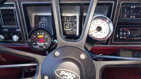 1978 Ford Bronco - Close-up interior shot of a 1978 Ford Bronco's dashboard, featuring a steering wheel with a Ford logo, an AEM air/fuel ratio gauge, and a S…