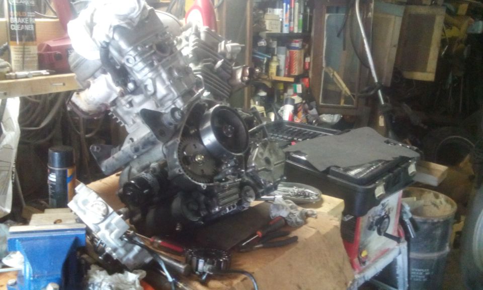 Disassembled motorcycle engine on a workbench with tools in a garage.