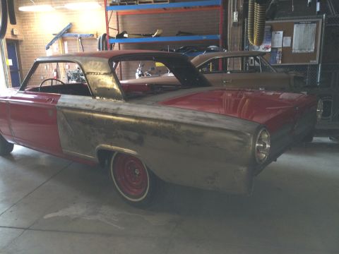 1964 Ford Fairlane - A classic car is in a garage, showing primer on its body panels and a red roof, with another vehicle parked behind it.