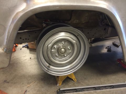 1964 Ford Fairlane - A vintage steel wheel is mounted on a jack stand, revealing the vehicle's chassis and wheel hub assembly.