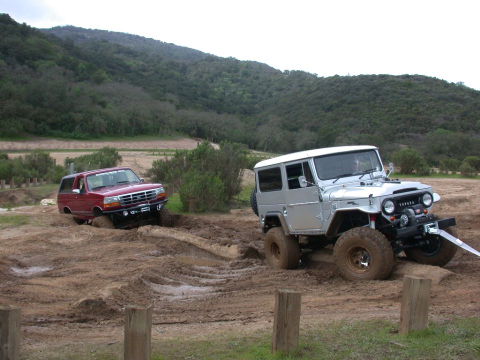 Red SUV stuck in mud next to a silver Toyota Land Cruiser on a dirt track