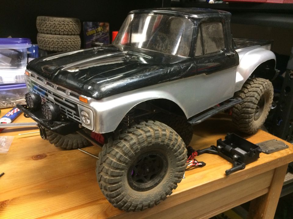 RC pickup truck with black and silver body, large tires, and front bumper lights on a wooden workbench.