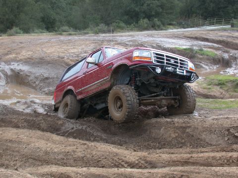 1996 Ford Bronco - A red 1996 Ford Bronco tackles a challenging muddy off-road course.