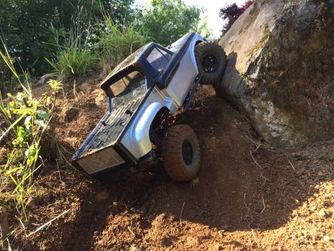 1989 Ford Bronco - This remote control truck is navigating a challenging off-road course, climbing a steep dirt incline beside a large rock formation.