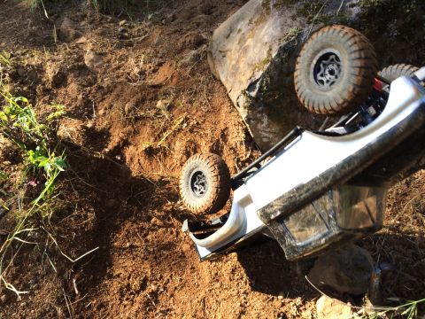 1989 Ford Bronco - An RC rock crawler is stuck on its side on a rocky, dirt trail.