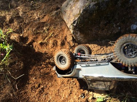 1989 Ford Bronco - A toy RC car is overturned on a dirt embankment near a large boulder.