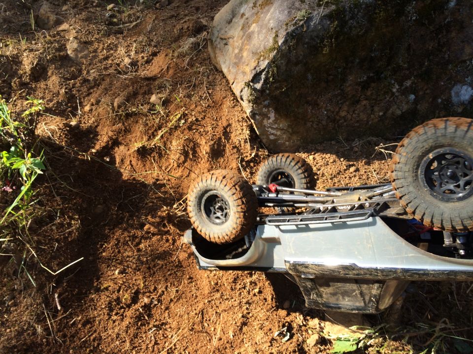 Toy RC car on its side in dirt next to a large rock