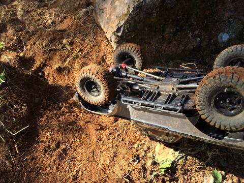 1989 Ford Bronco - An off-road vehicle has overturned on a dirt path, resting on its side near a large boulder.