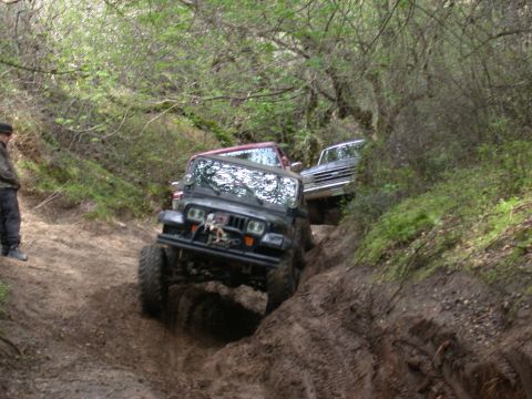 1996 Ford Bronco - Multiple off-road vehicles tackle a challenging muddy incline during an outdoor excursion.