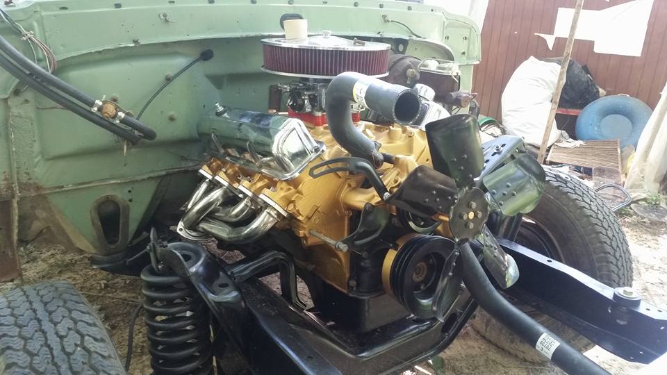 Engine bay of a light green vehicle with a yellow engine, chrome headers, and a large fan