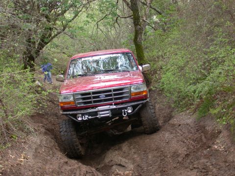 1996 Ford Bronco - This red 1996 Ford Bronco navigates a challenging muddy off-road path.