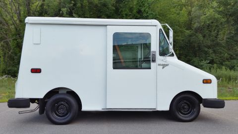 1991 Ford Crown Victoria LTD - A white Grumman LLV postal truck is parked on a paved surface with trees in the background.