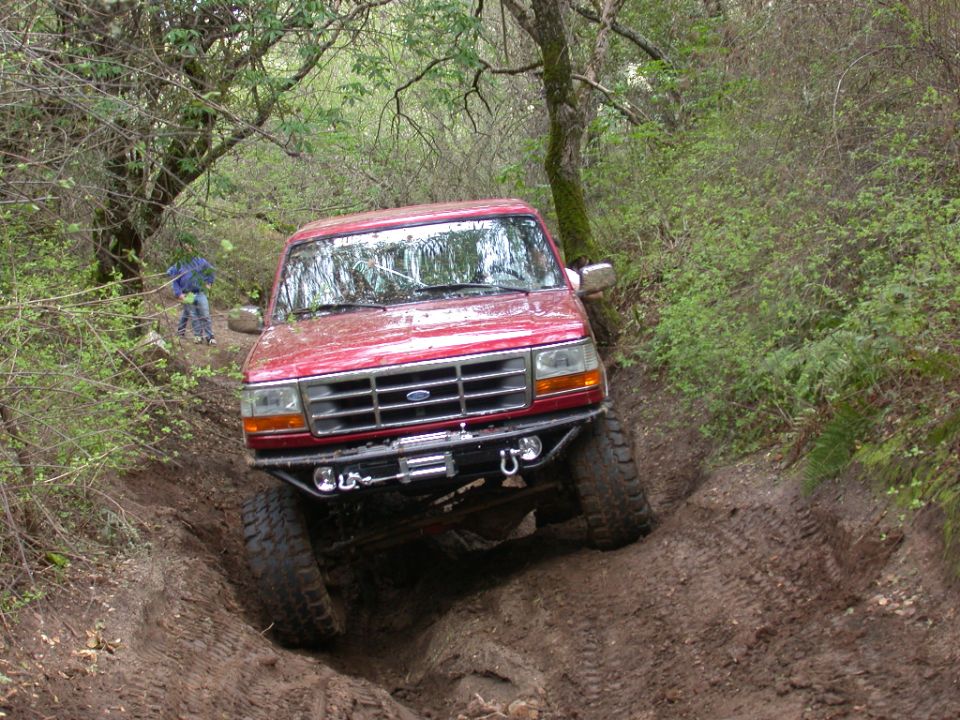 Red Ford truck with aftermarket bumper and winch navigating a muddy trail