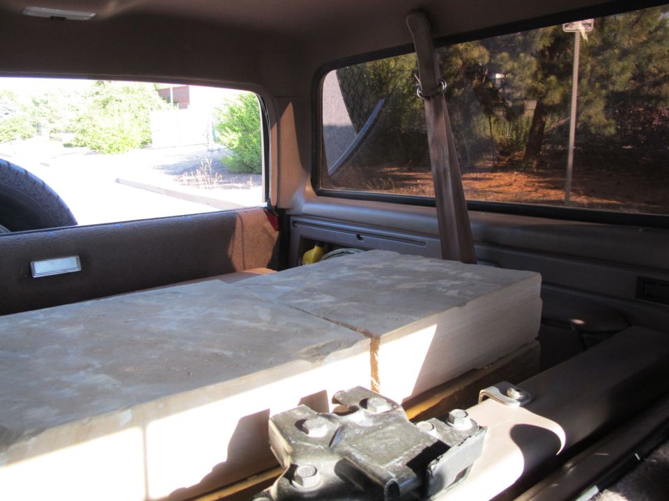 Inside of a vehicle, looking towards the rear. Large flat objects are loaded in the back. A spare tire is visible on the left