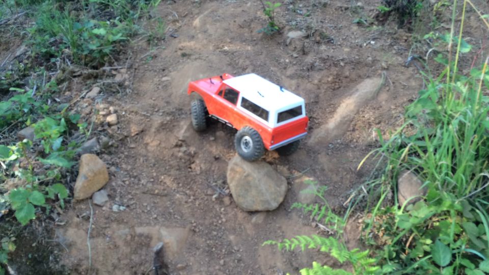 Red and white RC off-road truck on a dirt trail with rocks