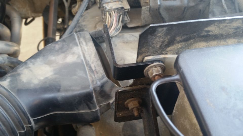 Black metal bracket bolted to engine bay components including air intake tube.