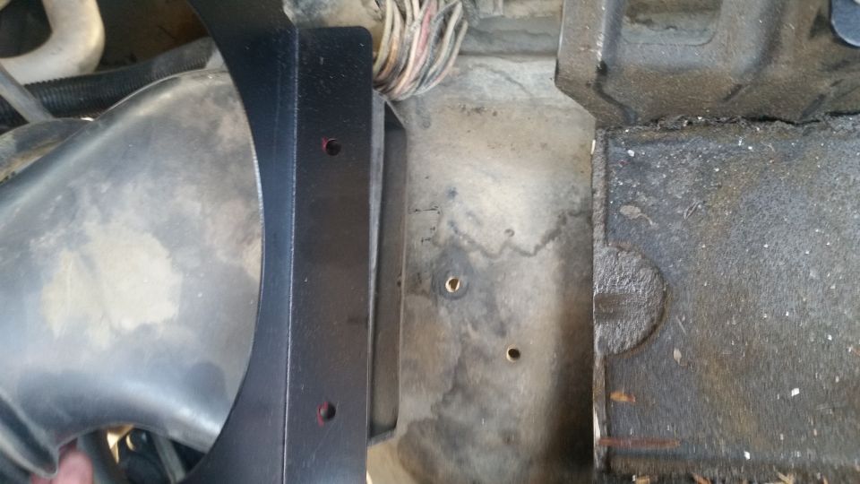Black metal bracket near silver air intake tube and wires in engine bay.