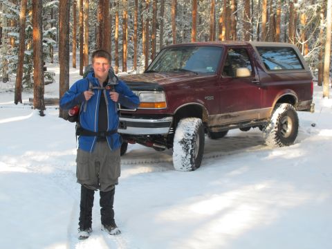 1996 Ford Bronco - A person stands in the snow in front of a maroon Ford Bronco with large tires. The vehicle is parked in a wooded area with snow on the grou…
