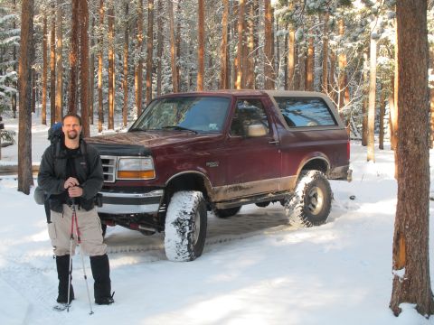 1996 Ford Bronco - A man stands in the snow next to a maroon Ford Bronco with a tan top. The vehicle is parked in a forest with snow-covered trees.