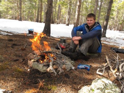 1996 Ford Bronco - A young man sits by a campfire in a snowy forest. He is wearing a blue jacket and gray pants, and is looking at the camera with a smile. A…