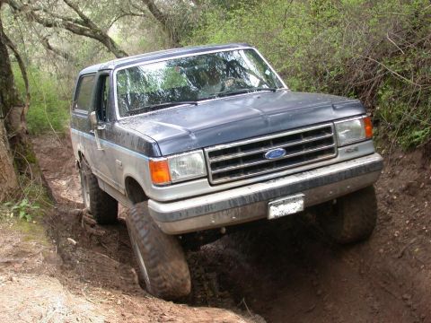1996 Ford Bronco - This Ford Bronco is navigating a challenging off-road path with steep inclines and loose dirt.