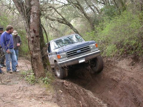 1996 Ford Bronco - A Ford Bronco navigates a challenging muddy off-road trail with onlookers present.