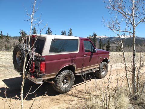 1996 Ford Bronco - Maroon 1996 Ford Bronco with a spare tire on the back, parked off-road with mountains in the distance.