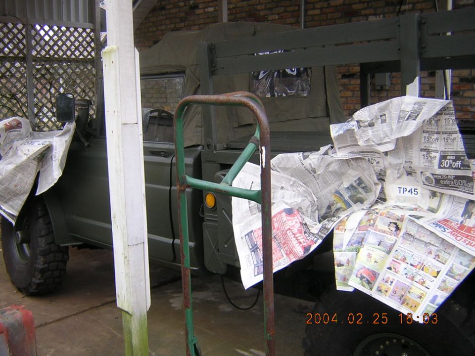 Olive green military truck side view, bed covered in newspaper