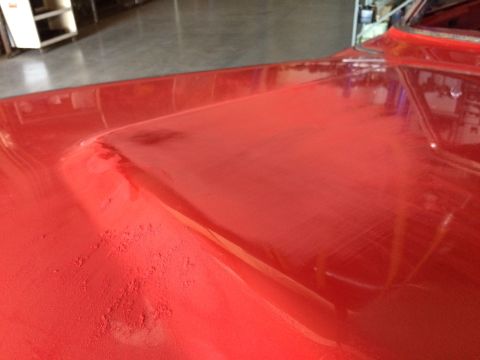 1964 Ford Fairlane - The hood of a red vehicle shows dust and minor imperfections, suggesting it's in a workshop.