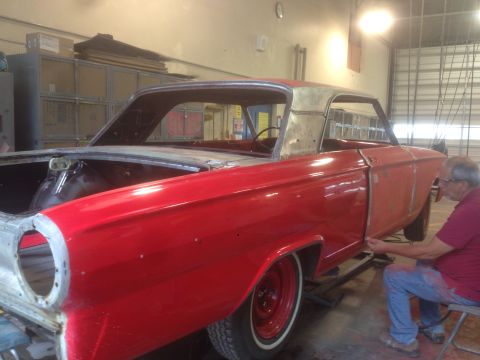 1964 Ford Fairlane - A man is working on the body of a red coupe, which appears to be a 1963 Ford Falcon, in a workshop setting.