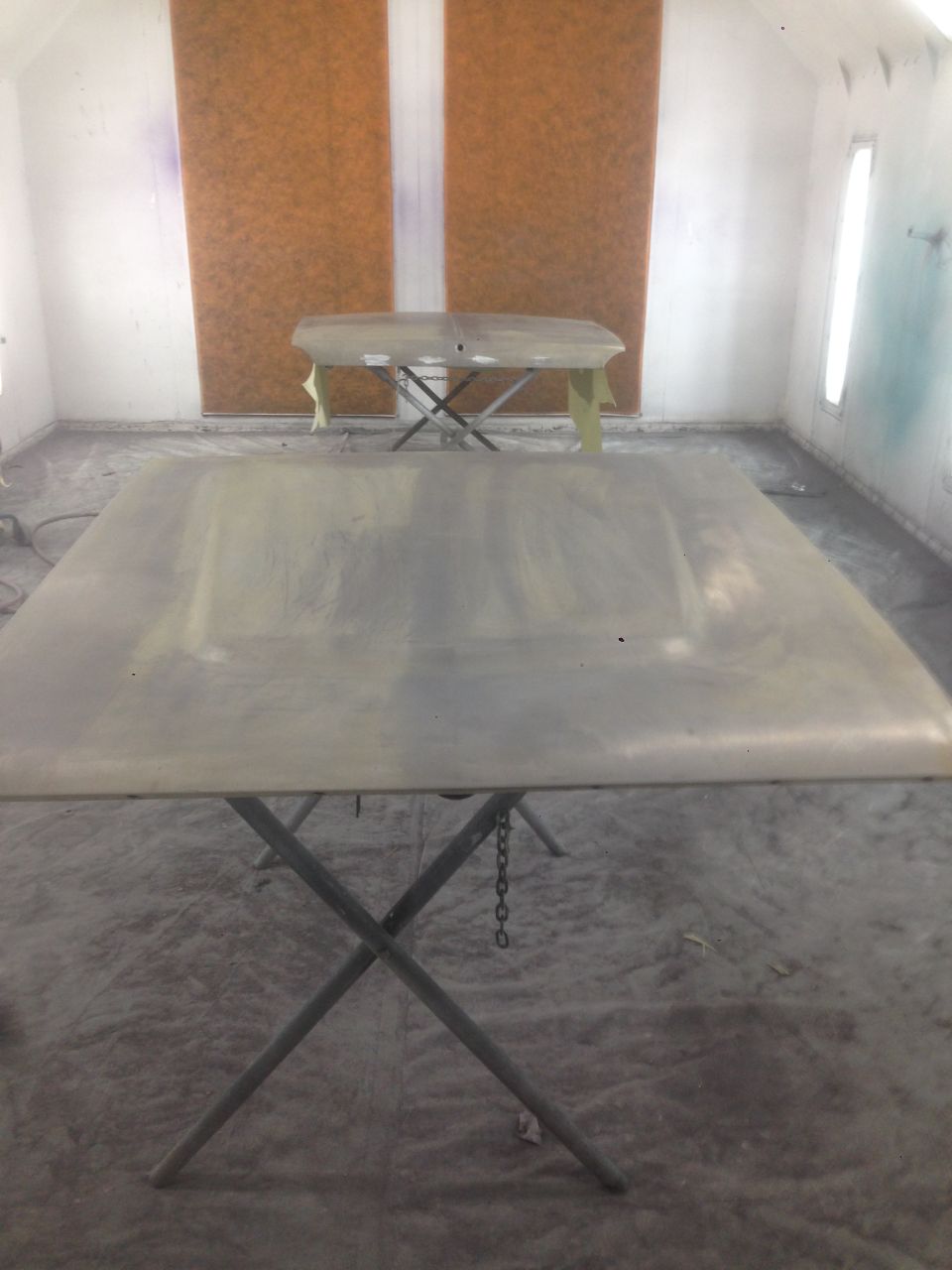 Two car hoods on stands in a paint booth