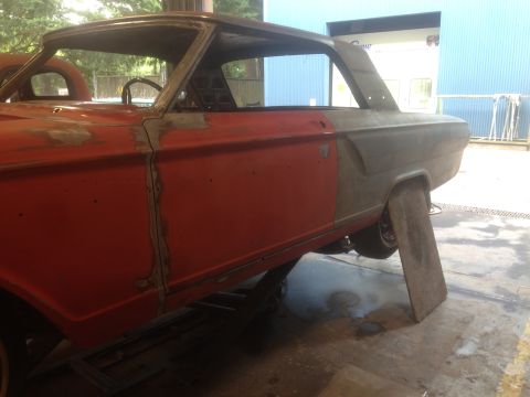 1964 Ford Fairlane - A classic car is undergoing repairs, showing its red door and gray rear quarter panel with visible bodywork.