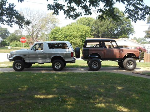 1972 Ford Bronco - Two Ford Broncos are parked side-by-side on a driveway, one silver and one showing rust.