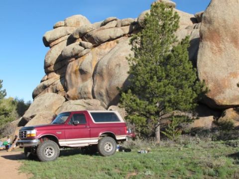 1996 Ford Bronco - A red 1996 Ford Bronco is parked in a grassy area with large rock formations in the background.