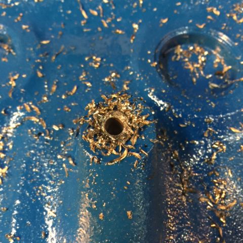 1978 Ford Bronco - A close-up view shows metal shavings scattered around a freshly drilled hole in a blue painted surface. The hole appears to be in a vehicle…