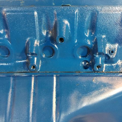 1978 Ford Bronco - A close-up view of a blue painted engine block with several bolt holes and mounting points visible.