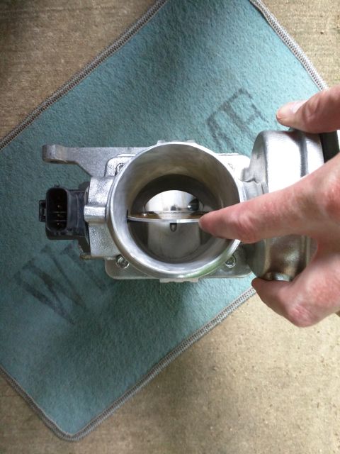 2007 Ford Crown Victoria - A person's hand is shown pressing on the throttle plate of a throttle body assembly. The assembly is silver and has a black electrical conn…