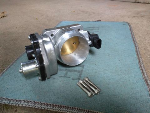2007 Ford Crown Victoria - A silver throttle body with a black connector and a silver actuator is shown on a teal mat. Three silver bolts are placed in front of the t…