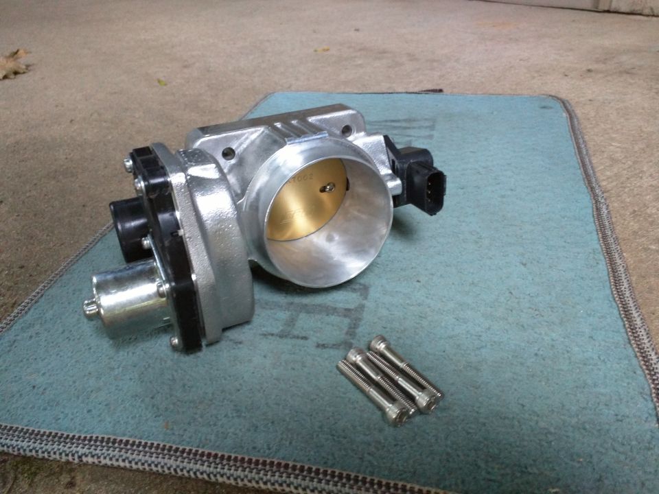 Silver throttle body with black connector and actuator, on a teal mat with three bolts.