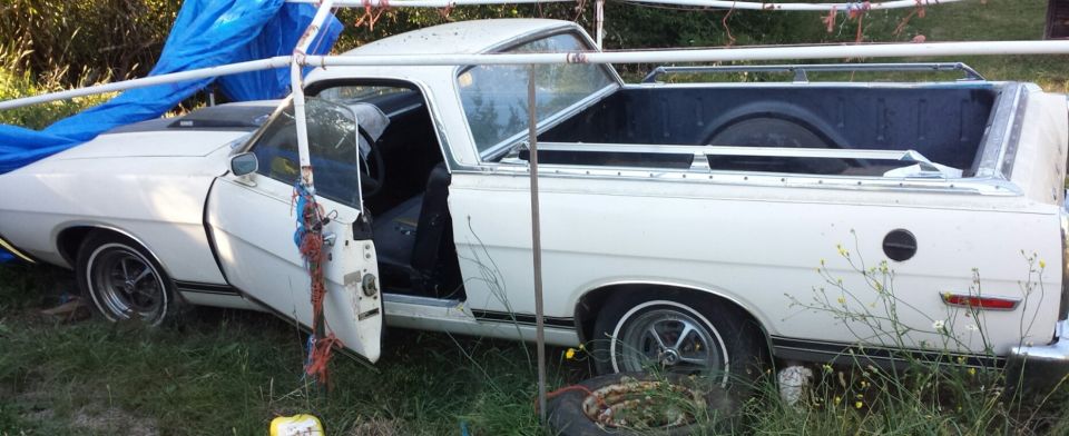 White 1969 Ford Ranchero with driver's door open, partially covered by a blue tarp.