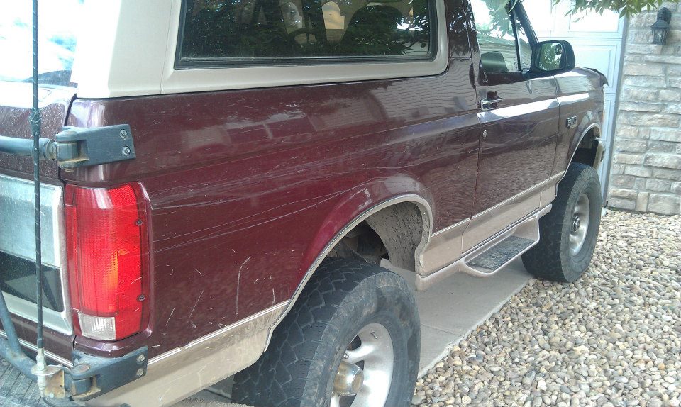 1996 Ford Bronco rear driver's side, dark red with tan trim, parked on gravel.