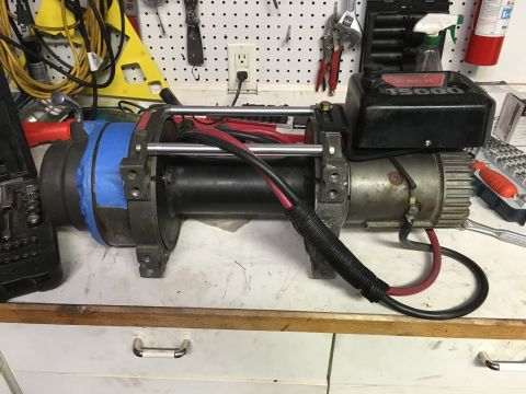 1996 Ford Bronco - A Warn 15000 winch is shown on a workbench. The winch has red and black power cables connected and is partially wrapped in blue tape on one…