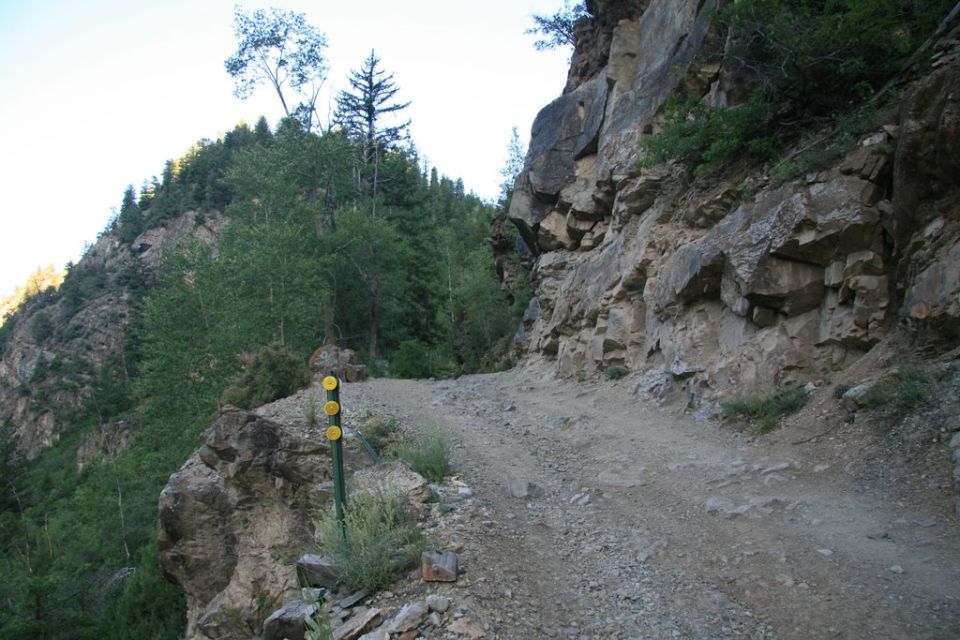 A rocky mountain trail next to a cliff with a trail marker.
