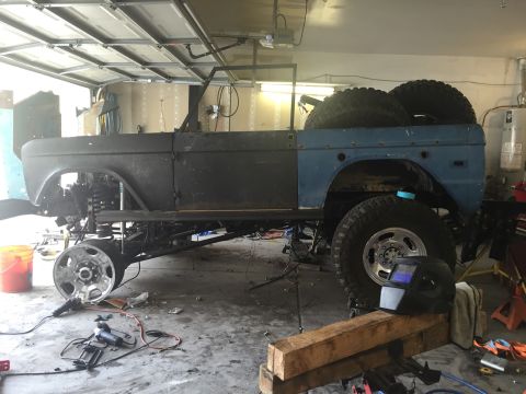 1979 Ford Bronco - A partially disassembled 1979 Ford Bronco is shown in a garage setting, with the body stripped down and undergoing modifications. Tools and…