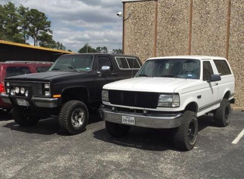 1996 Ford Bronco - A black Chevrolet K5 Blazer and a white Ford Bronco are parked side-by-side in a parking lot.