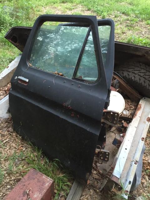 1996 Ford Bronco - A black driver's side truck door with a window is propped open and leaning against other scrap metal parts. The door has a silver door hand…