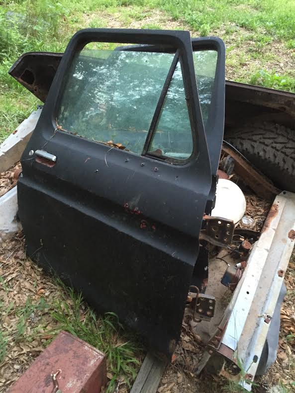 Black truck door with window, silver handle, and rust spots, leaning on scrap metal.