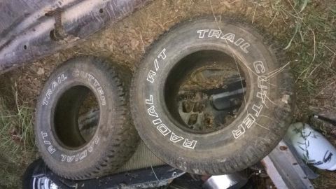 1996 Ford Bronco - Two off-road tires with white lettering are laid on the ground next to a vehicle's undercarriage. The tires read "TRAIL CUTTER" and "TRAIL…