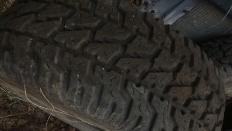 1996 Ford Bronco - A close-up view of a dark-colored tire with a rugged tread pattern, likely from an off-road vehicle. The tire is resting on the ground amon…