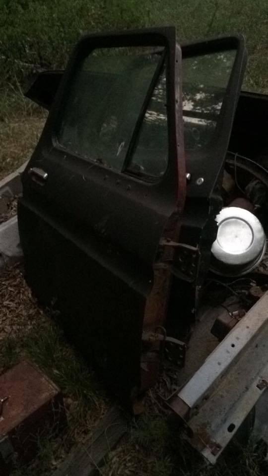 Detached driver's side door of a dark vehicle, revealing interior and engine parts.